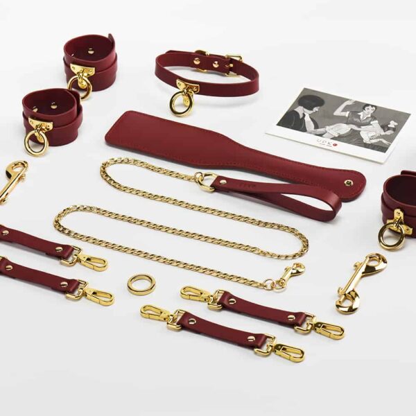 BDSM Accessoires aus bordeauxrotem Leder und Details aus 24K Gold, Hand-, Fuß- und Beinfesseln und Halsband und Leine, UPKO Spanking Paddle bei Brigade Mondaine