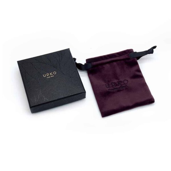 Kleine schwarze Upko-Box mit Graffiti mit ihrem kleinen Beutel aus dunklem bordeauxrotem Samt und bestickt mit schwarzem Garn mit dem UPKO-Logo für die limitierten Editionen UPKO X Brigade Mondaine auf weißem Hintergrund erhältlich bei Brigade Mondaine