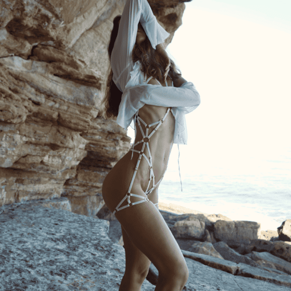 COUTURE DE NUIT - Traje Grace Exclusivo Blanco Fotografía de una mujer frente a unas rocas, vestida con un arnés blanco con detalles dorados y una camisa blanca