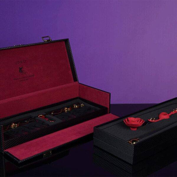 schwarzer Koffer mit rotem Innenleben. Darin befinden sich schwarze Upko-Accessoires und eine rote Ball-Gang-Rose.