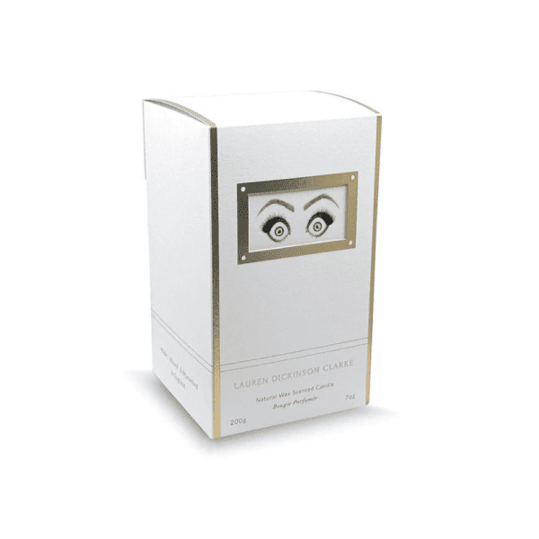 LDC - Performer Bougie Parfumée Le packaging de la bougie arbore une couleur blanche avec des touches dorées, et il est agrémenté d'un motif représentant des yeux exprimant de l'étonnement.