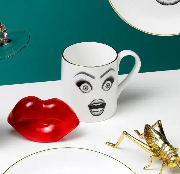 LDC - Performer Tasse à café Une tasse en porcelaine chinoise blanche présente un dessin en feutrine noire illustrant un visage surpris avec des yeux très choqués et une bouche ouverte, le tout rehaussé de détails dorés.