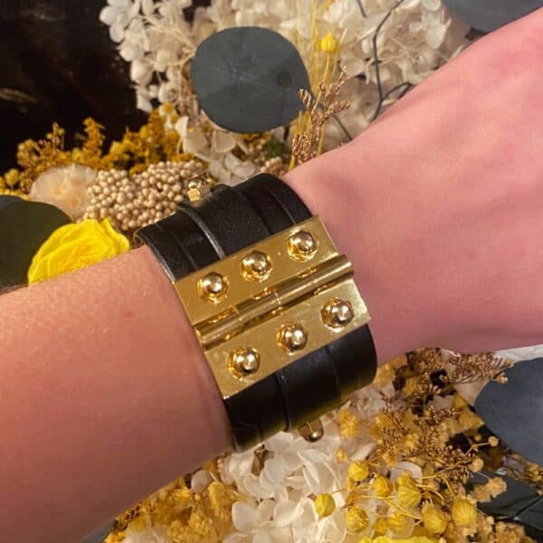 UNA BURKE - Scharnierarmband mit doppeltem Riemen Scharnierarmband mit Doppelriemen aus schwarzem Leder, verstellbar von 17 bis 20 cm. Handgefertigt von Úna Burke in Irland aus vollnarbigem Rindsleder und goldbeschichtetem Messing. Schickes und langlebiges Rock-Design.