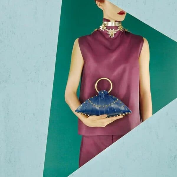 UNA BURKE - Sac Shell Blueberry Femme portant un sac à main Une burke en cuir bleu sur un fond bleu turquoise.