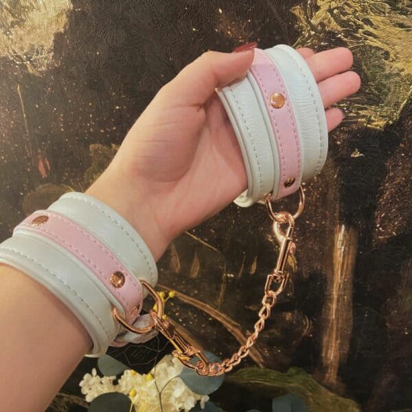 Esposas FAIRY bondage de cuero blanco y rosa con detalles en oro rosa. Ajustable con hebillas de metal y clips de liberación rápida para un ajuste seguro y cómodo. Perfectas para juegos BDSM.