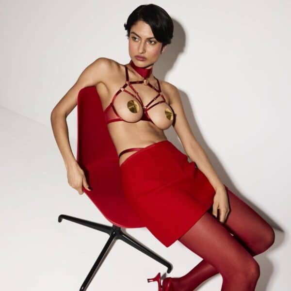 Mujer sentada con un sujetador abierto de estilo bondage en color rojo.