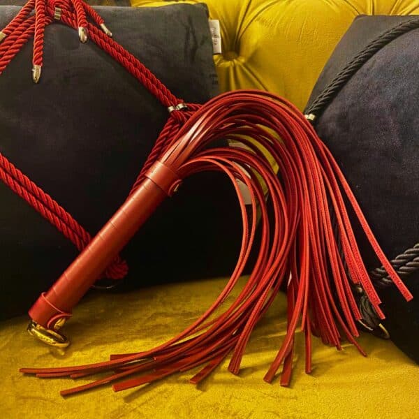 Fouet rouge BDSM posé sur un fauteuil.