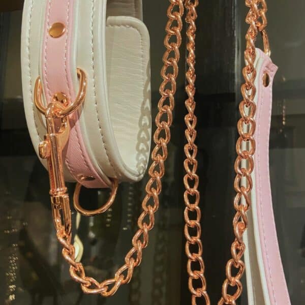 BDSM-Halskette FAIRY aus weißem und pastellrosa Leder mit passender Leine aus Roségold. Bequem, verstellbar und raffiniert. Dieses hochwertige Bondage-Accessoire ist bei Brigade Mondaine erhältlich.