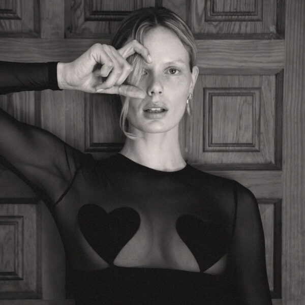 UNDRESS CODE - Lecho de Rosas Detalle de una foto en blanco y negro de una mujer sentada de frente con un body negro de rejilla de manga larga