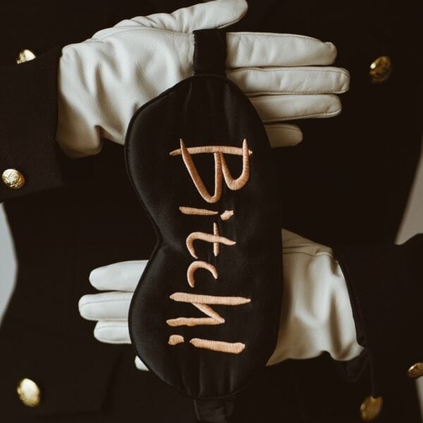 Masque de nuit UPKO en velours noir brodé Bitch Please, présenté avec des gants blancs, disponible chez Brigade Mondaine Paris