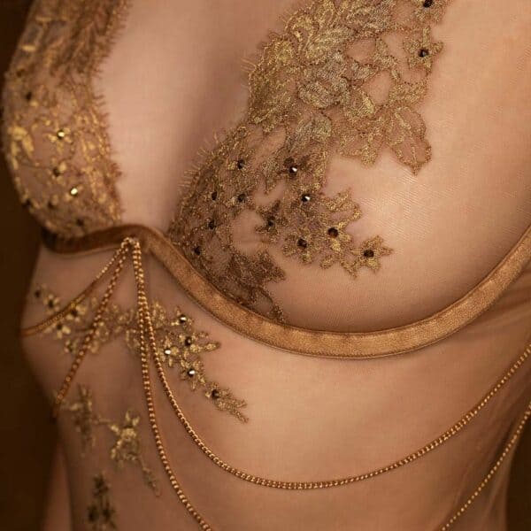 Hervé by Céline Marie Lingerie de Luxe BRIGADE MONDAINE (29) Detail of a 3/4-length woman wearing a flesh-colored bodysuit with gold embroidery.