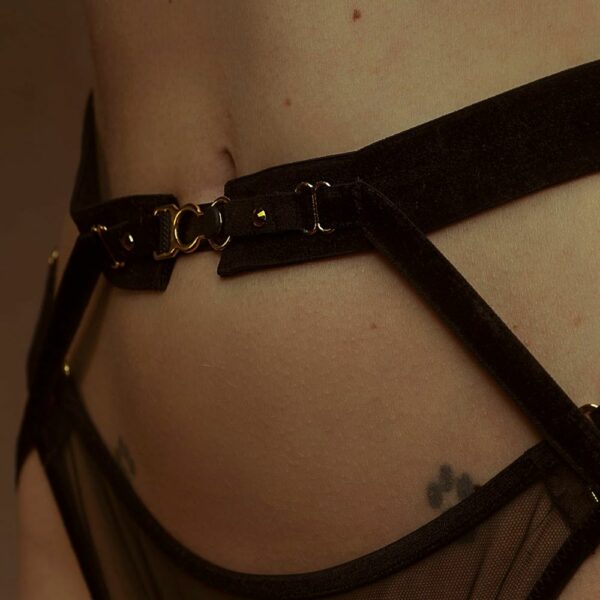 Nahaufnahme einer Frau in Dreiviertelansicht, die einen Netz-String und Strumpfhalter aus schwarzen, elastischen Samtbändern trägt