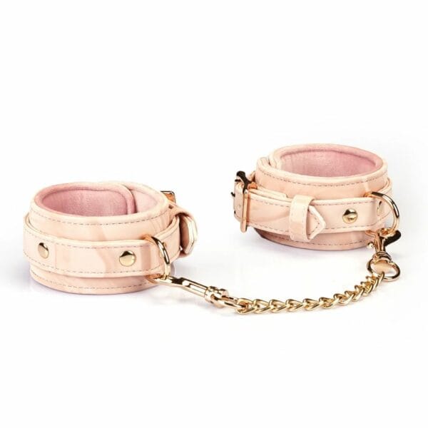 Boudoir Amor handcuffs in pastel pink and black vegan imitation leather. Gold-plated finish, D-ring for fastening. Adjustable buckles and quick-release clips for security and comfort. Ideal for elegant submission play.