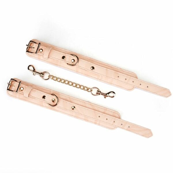 Boudoir Amor handcuffs in pastel pink and black vegan imitation leather. Gold-plated finish, D-ring for fastening. Adjustable buckles and quick-release clips for security and comfort. Ideal for elegant submission play.