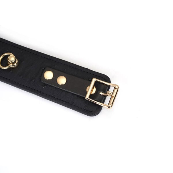 Produktfoto: Handfesseln aus schwarzem Leder und goldener Kette mit Verzierung am Befestigungsriemen mit goldener Schnalle
