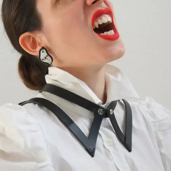 NIAR House - Choker 86647 Nahansicht des Chokers 86647 aus schwarzem Leder, der über einem weißen Hemd mit Kragen getragen wird, wobei das vom Hemdkragen inspirierte Design hervorgehoben wird. Die Frau trägt roten Lippenstift und zeigt leicht vampirische Zähne, was ihrem Look einen gewagten Touch verleiht.