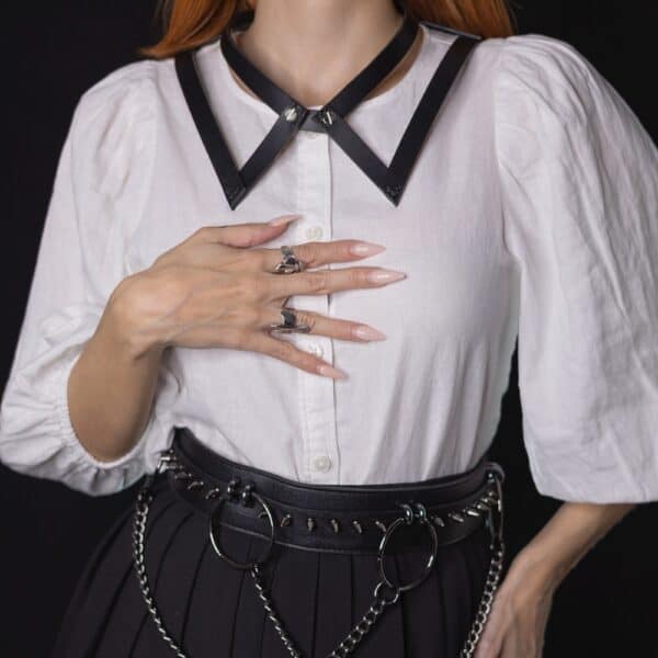 NIAR House - Choker 86647 Choker 86647 aus schwarzem Leder, getragen mit einem weißen Hemd und einem schwarzen Rock mit silbernen Details. Handgefertigt, mit Schrauben an der Vorderseite, die an die Knöpfe eines Kragens erinnern, und einer verstellbaren Schnalle an der Rückseite.