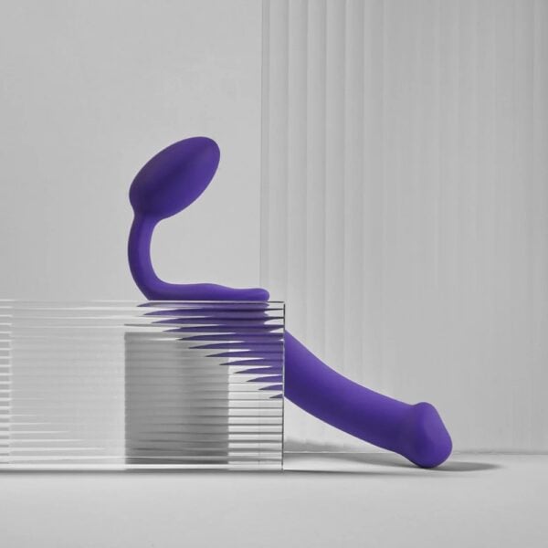 STRAP-ON-ME Strap-on original violet – Sélection Brigade Mondaine Paris Plug strapless violet STRAP-ON-ME au design courbé et ergonomique, posé sur un socle minimaliste, sélection Brigade Mondaine Paris.