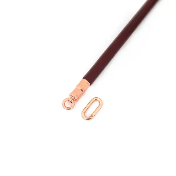 Spreizstange aus weinrotem Leder mit einem Kern aus Eukalyptusholz. O-Ringe aus roségoldfarbenem Metall zur Befestigung von Knöchelschienen. Elegant und funktional für raffinierte BDSM-Spiele.
