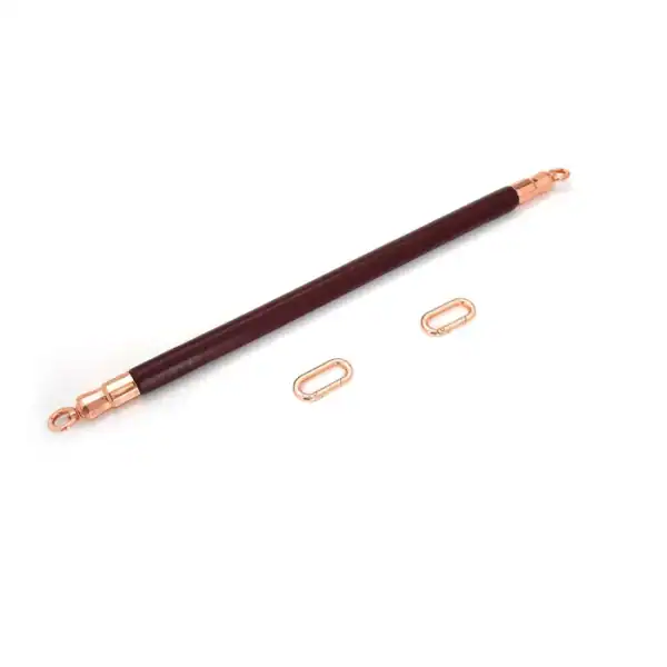 Spreizstange aus weinrotem Leder mit einem Kern aus Eukalyptusholz. O-Ringe aus roségoldfarbenem Metall zur Befestigung von Knöchelschienen. Elegant und funktional für raffinierte BDSM-Spiele.