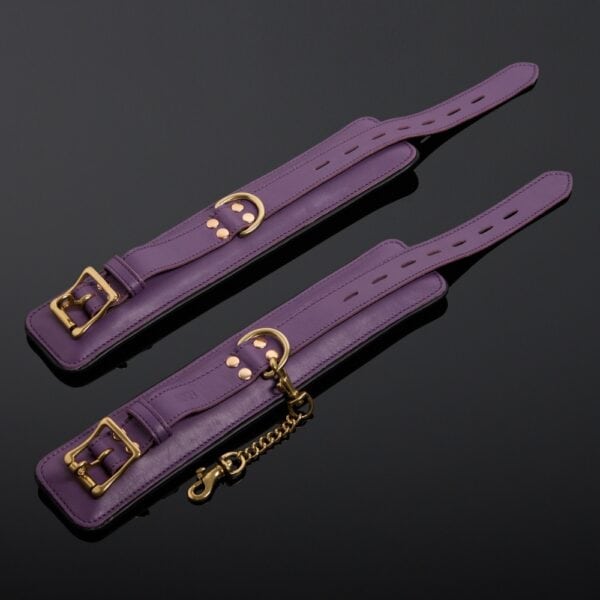 Esposas de piel de vaca violeta con doble cadena de mosquetón chapada en oro y cierre de hebilla ajustable.