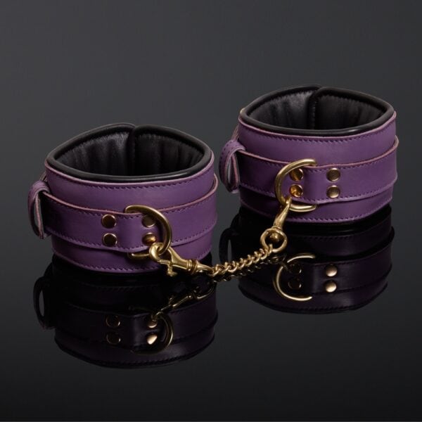 Esposas de piel de vaca violeta con doble cadena de mosquetón chapada en oro y cierre de hebilla ajustable.