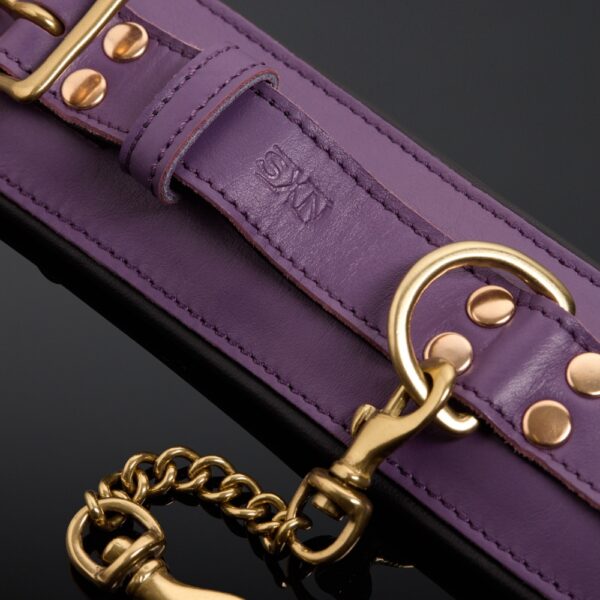 Esposas de piel de vaca violeta con doble cadena de mosquetón chapada en oro y cierre de hebilla ajustable.