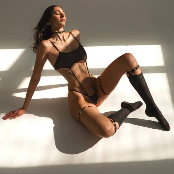 QRUCIFIX - GIA Stocking Harness - STELLA Garters - IVY Body Harness Black harness body in double apex tulle linked to an integrated mesh g-string and high neckline with 18-carat gold-plated details Sculpting mid-leg stockings in stretch tulle, with adjustable straps and 18-carat gold-plated Zamac finish and Black thigh-high garters in recycled polyamide with 18-carat gold-plated Zamac components and Kemtex non-toxic dyes.