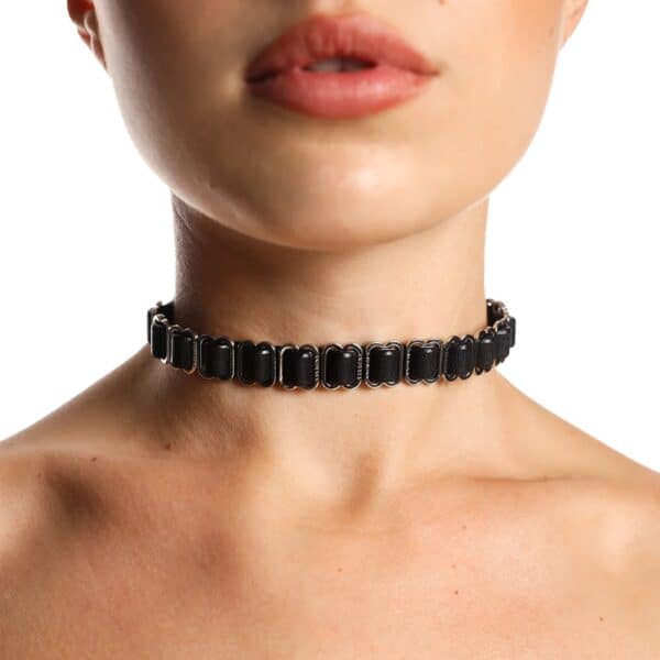 Black ANOESES choker worn around the neck of a female model, featuring aligned metal rings and an adjustable structure, high-end fetish aesthetic Brigade Mondaine Paris.