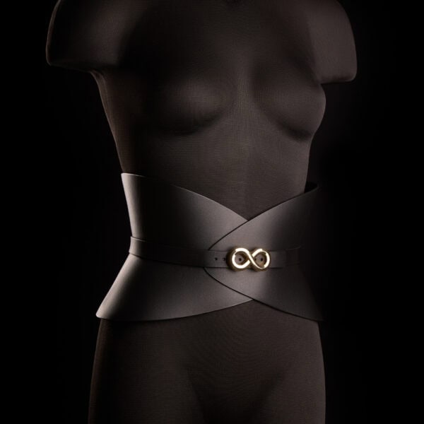 Corset ceinture HUDIA IINFYNII en cuir noir avec fermoir métallique infini porté sur un tailleur noir, accessoire structurant et graphique proposé par Brigade Mondaine Paris