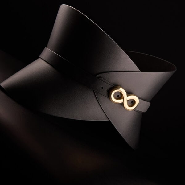 Corset ceinture HUDIA IINFYNII en cuir noir avec fermoir métallique infini porté sur un tailleur noir, accessoire structurant et graphique proposé par Brigade Mondaine Paris
