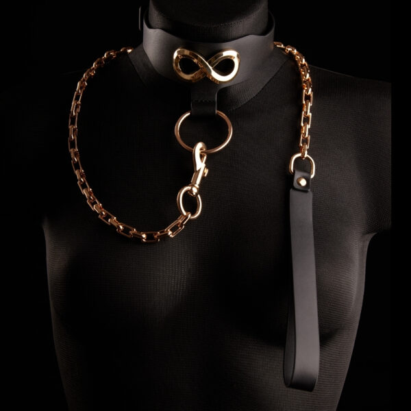 Halsband Leine SEVERA IINFYNII - Brigade Mondaine Paris Die Leine SEVERA von IINFYNII kombiniert schwarzes Leder und eine goldene Metallkette in einer selbstbewussten und strukturierenden Konstruktion. Sie ist als starkes Körperteil gedacht und besteht aus einem Lederhalsband, das mit einem Signatur-Metallsymbol verziert ist und durch eine Gelenkkette verlängert wird, die mit einem zentralen Ring verbunden ist. Es ist anpassbar und kann allein getragen oder in eine komplette Silhouette integriert werden, zwischen Schmuckstück mit Zwangscharakter und skulpturalem Accessoire. Ein grafisches, direktes Stück, das für diejenigen entworfen wurde, die ihren Körper als ein Feld des Ausdrucks betrachten.