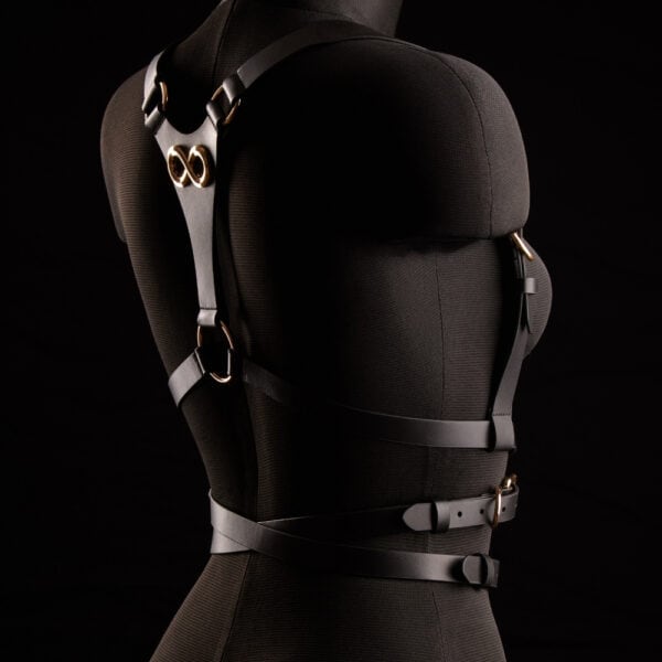 TRISCA IINFYNII harness in black webbing with gold buckles and central detail, structuring accessory worn on the bust proposed by Brigade Mondaine Paris