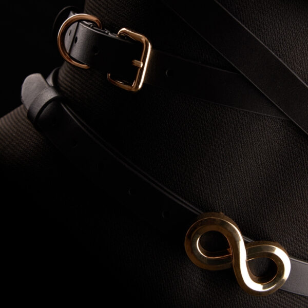 TRISCA IINFYNII harness in black webbing with gold buckles and central detail, structuring accessory worn on the bust proposed by Brigade Mondaine Paris