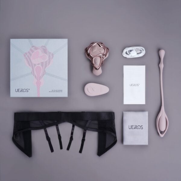 Complete UEROS vibrator with harness, accessories, remote control, charging cable and packaging, presented flat on gray background.