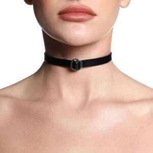 ANOESES necklace in black leather presented flat, thin band with central metal ring and adjustable snap closure, high-end fetish aesthetic Brigade Mondaine Paris.