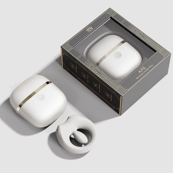 APIS connected cockring presented with its charging case, USB cable and warranty card, set against a light background in a minimalist, elegant setting.
