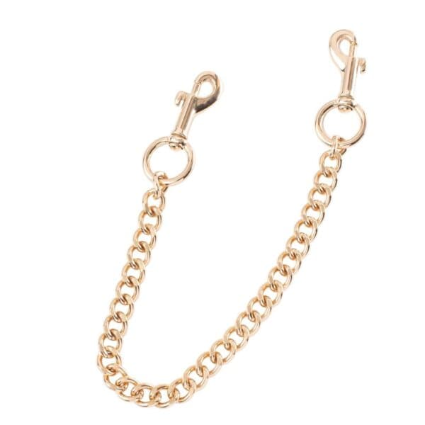 Esposas tobilleras premium en cuero negro | Brigade Mondaine Par de tobilleras de piel negra unidas por una cadena dorada, con hebillas metálicas ajustables y meticulosamente acabadas, presentadas sobre un fondo blanco de estética refinada.
