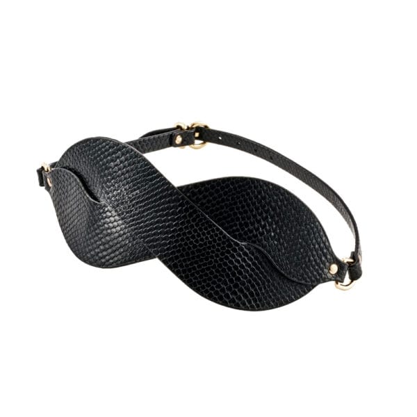 Masque BDSM en cuir noir texturé à la forme enveloppante, avec attaches réglables et bouclerie dorée, présenté sur fond noir dans une mise en scène élégante et minimaliste.