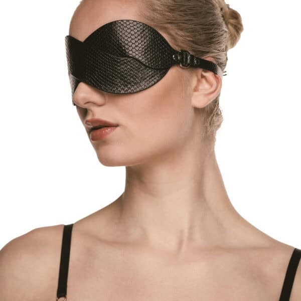 Masque BDSM en cuir noir texturé à la forme enveloppante, avec attaches réglables et bouclerie dorée, présenté sur fond noir dans une mise en scène élégante et minimaliste.