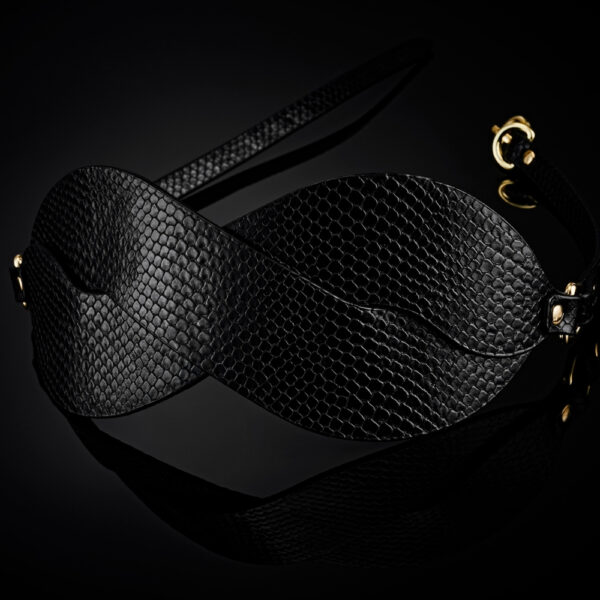 Masque BDSM en cuir noir texturé à la forme enveloppante, avec attaches réglables et bouclerie dorée, présenté sur fond noir dans une mise en scène élégante et minimaliste.