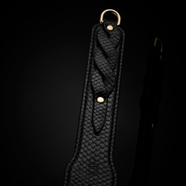 Model trägt einen transparenten schwarzen Body und hält ein BDSM-Paddle aus schwarzem Leder mit strukturiertem Finish. Fotografiert vor einem weißen Hintergrund in einer schlichten und eleganten Inszenierung.