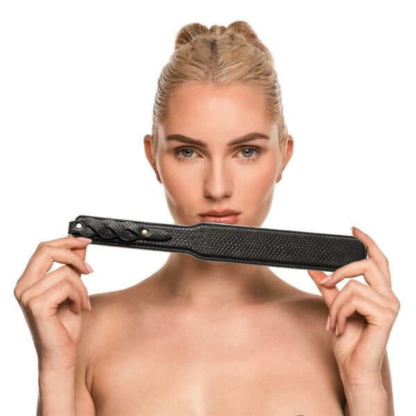 Model trägt einen transparenten schwarzen Body und hält ein BDSM-Paddle aus schwarzem Leder mit strukturiertem Finish. Fotografiert vor einem weißen Hintergrund in einer schlichten und eleganten Inszenierung.