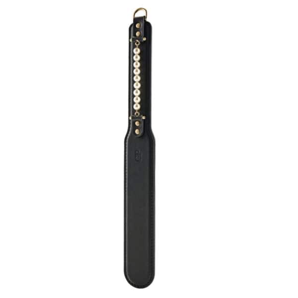 Paddle BDSM en cuir noir avec finition lisse et rangée de perles décoratives, tenu par un modèle en studio, accessoire sélectionné par Brigade Mondaine Paris.