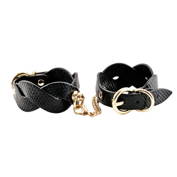 Modèle portant des menottes BDSM noires pour poignets avec chaîne dorée, accessoire de contrainte proposé par Brigade Mondaine Paris.