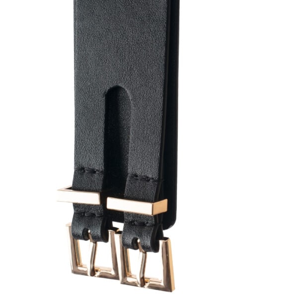 Esposas tobillo BDSM cuero negro y cadena de oro | Brigade Mondaine Esposas tobilleras BDSM de cuero negro con hebilla metálica y cadena dorada, llevadas en los tobillos con zapatos de tacón negros, fotografiadas sobre fondo gris.