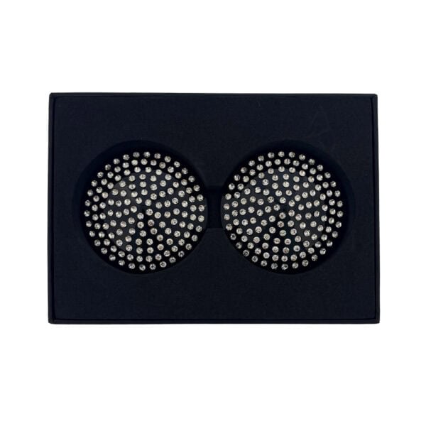 A pair of circular black nipple covers adorned with sparkling rhinestones, presented in a black case on a white background, with an elegant, minimalist aesthetic.