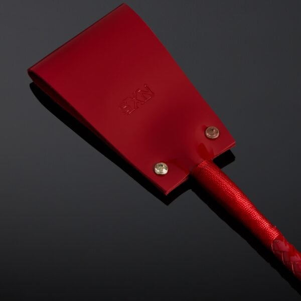 Cravache en vernis rouge HOUSE OF SXN avec manche rigide et extrémité plate, accessoire BDSM haut de gamme proposé par Brigade Mondaine Paris.