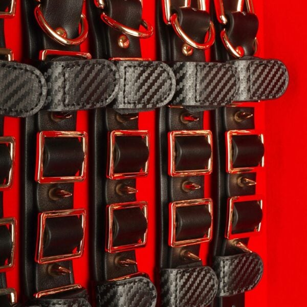 Caja BDSM abierta de cuero negro con interior rojo, que incluye un conjunto de accesorios variados como esposas, correas, fustas y cadenas, ordenados en una estética de lujo.