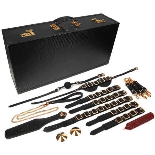 Caja BDSM abierta de cuero negro con interior rojo, que incluye un conjunto de accesorios variados como esposas, correas, fustas y cadenas, ordenados en una estética de lujo.
